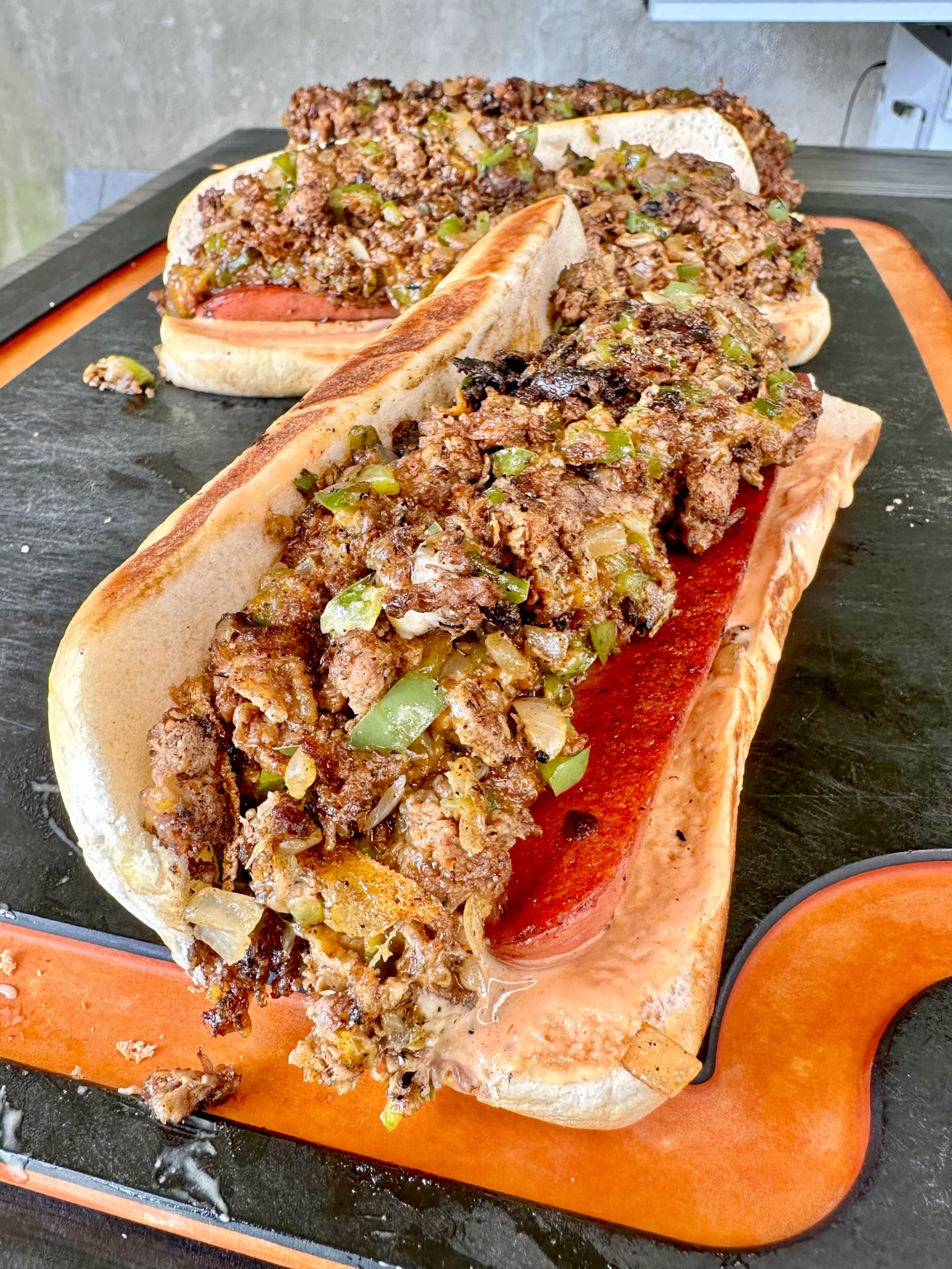 cheesesteak loaded hotdogs on a Cutting board