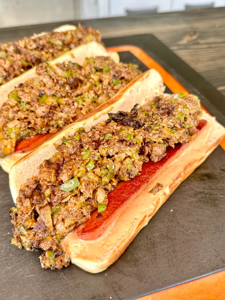angled loaded hot dogs on a cutting board covered in cheesesteak