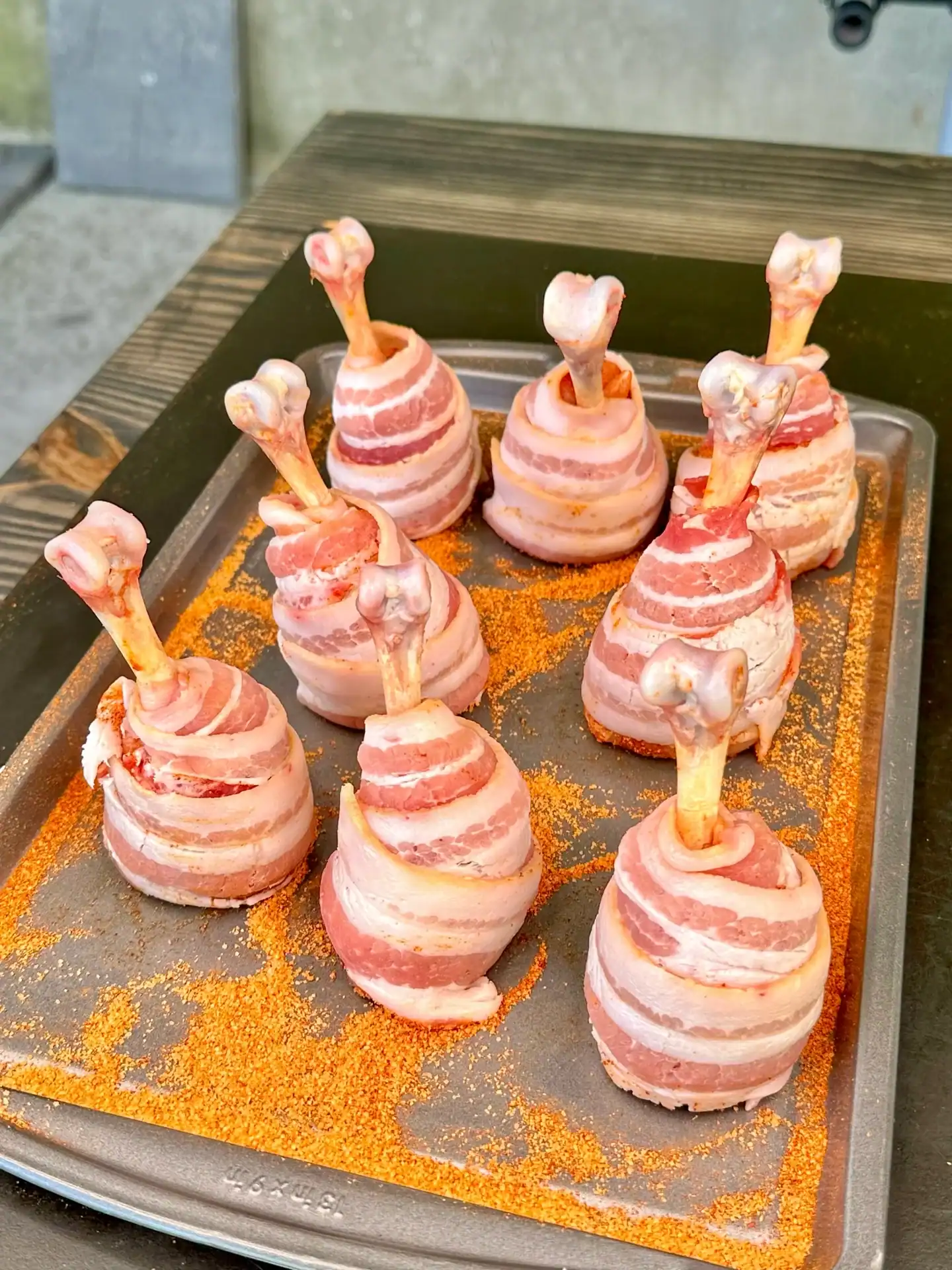Seasoned chicken lollipops wrapped in bacon before smoking