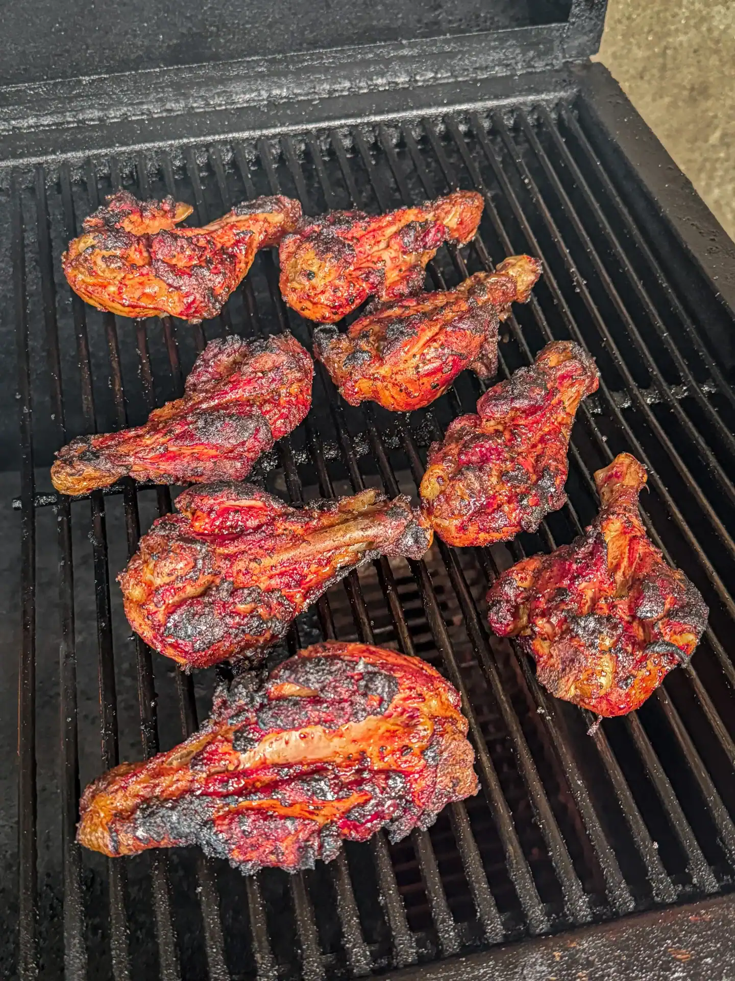charred chicken drumsticks being cooked over indirect heat on a grill.