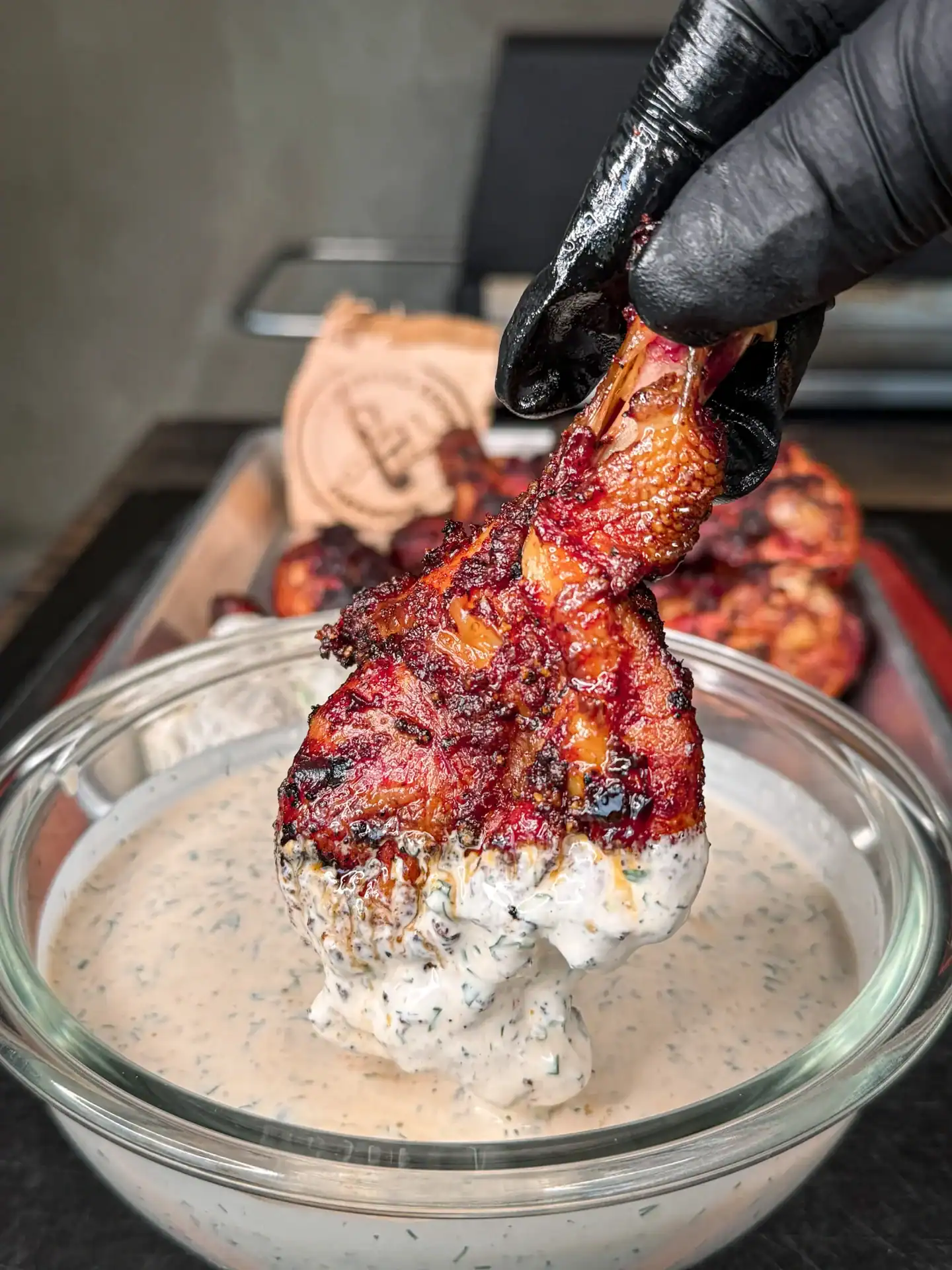 a single grilled butterflied chicken drumstick being dunked in a bowl filled with Chipotle ranch sauce.