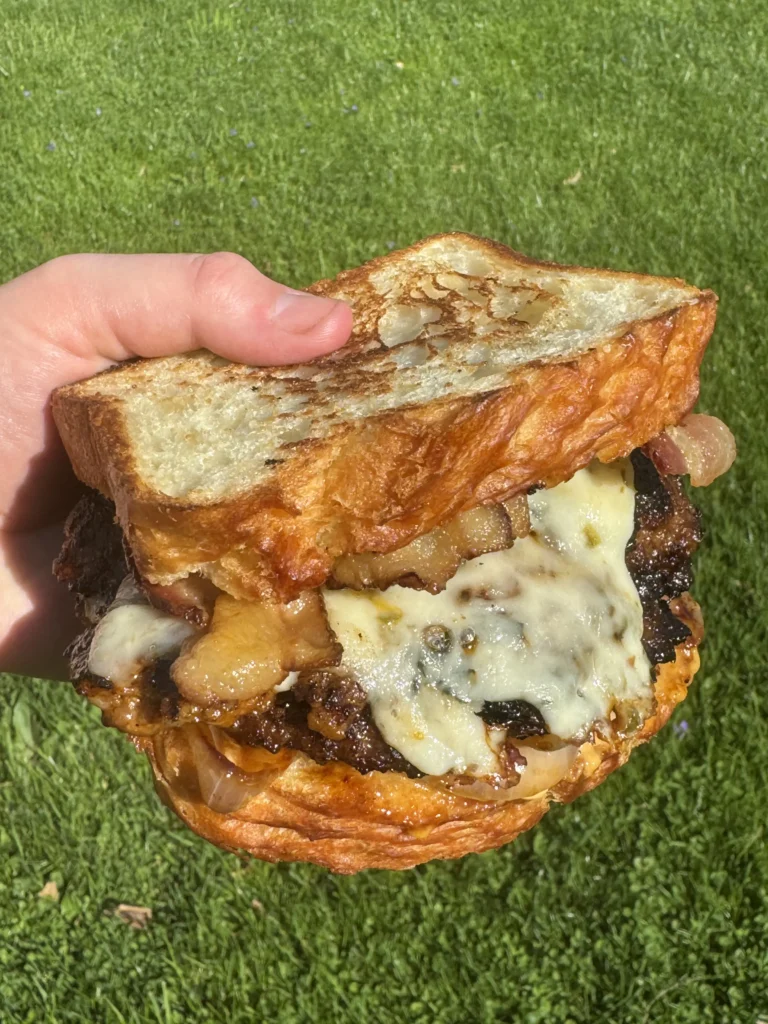 patty melt being held over grass