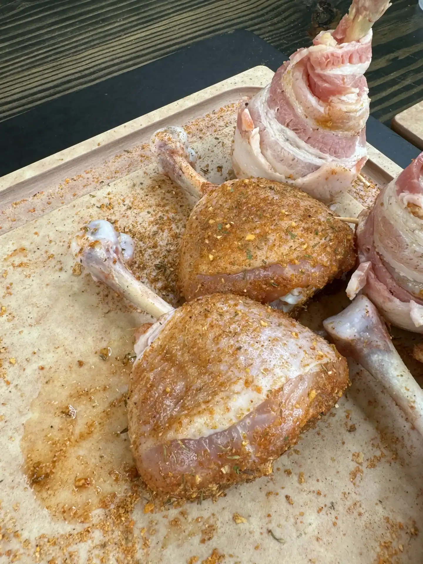 Chicken lollipops coated with BBQ seasoning on a baking sheet, ready to be wrapped in bacon smoked.