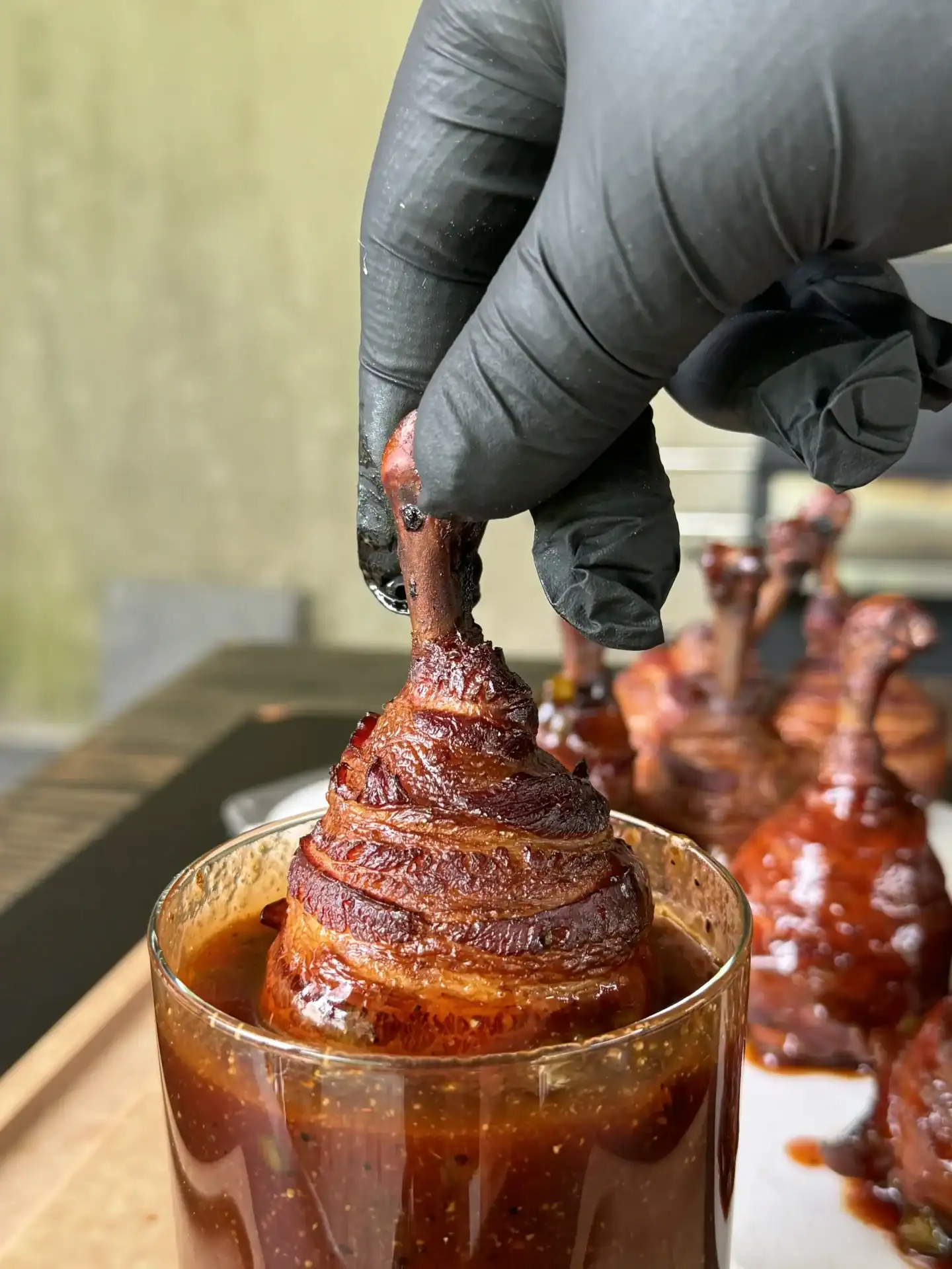 Bacon-wrapped chicken lollipop being dipped into homemade honey jalapeño BBQ sauce before the final smoke.