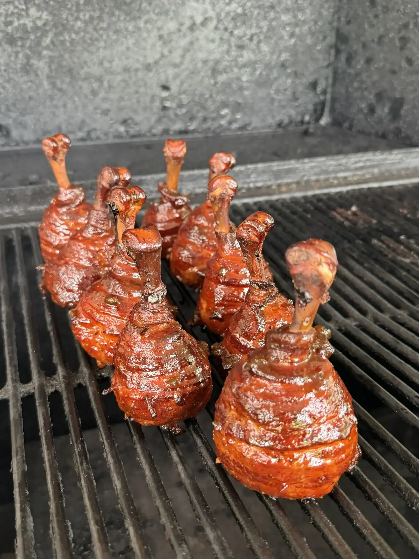 Honey jalapeño chicken lollipops standing upright on smoker grates with a glossy red BBQ glaze.