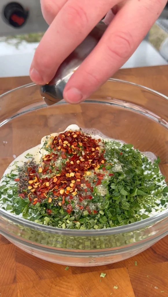 Homemade ranch dressing being whisked in a bowl with fresh herbs and buttermilk.