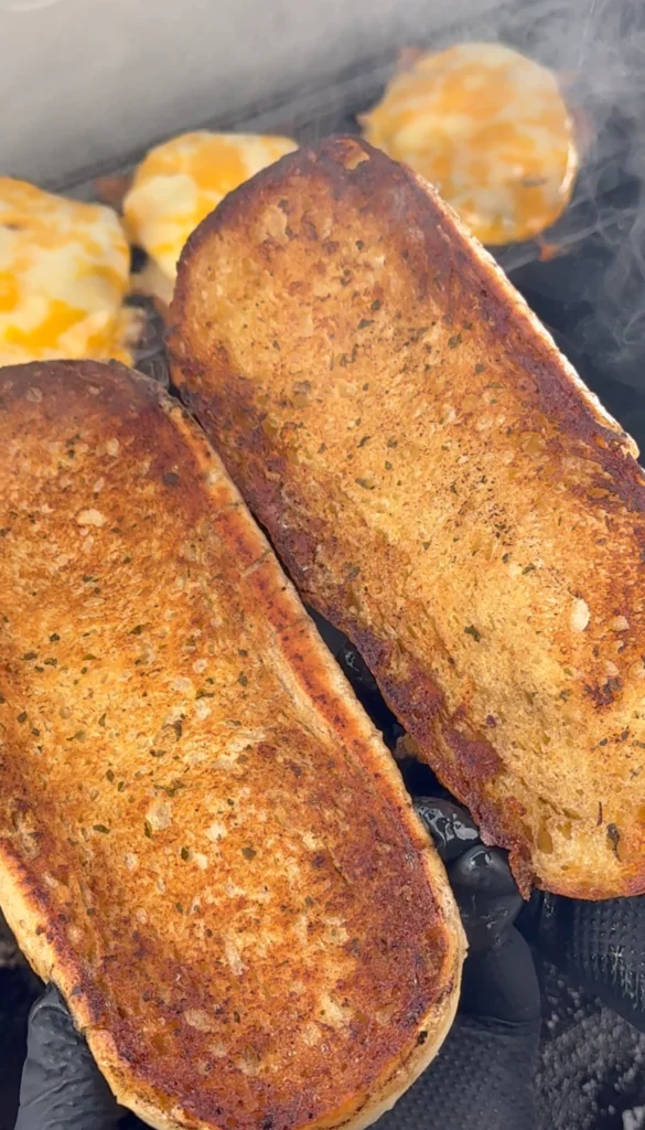 Toasted sandwich rolls on a griddle, golden brown and ready for assembling.