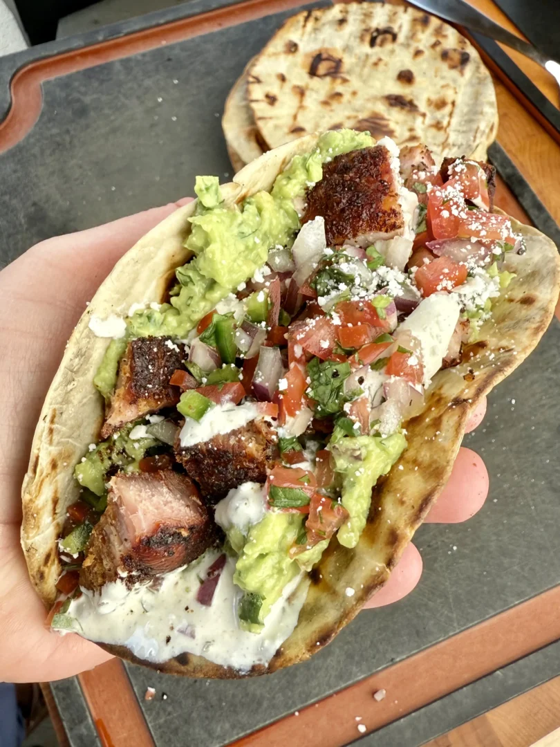 Hand holding a crispy chicharrón taco filled with guacamole and pico de gallo