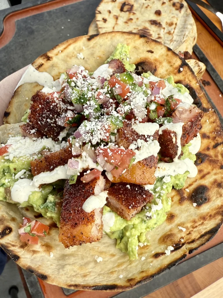 Garnished tacos served on a rustic plate with fresh cilantro and a side of lime wedges