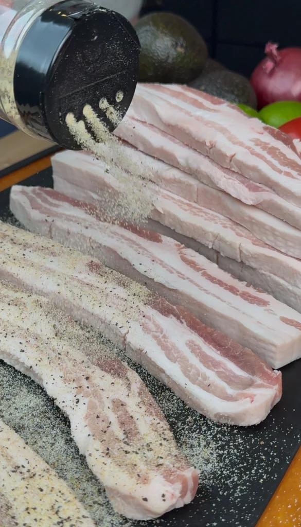 Seasoning pork belly with salt, pepper, and garlic powder before smoking