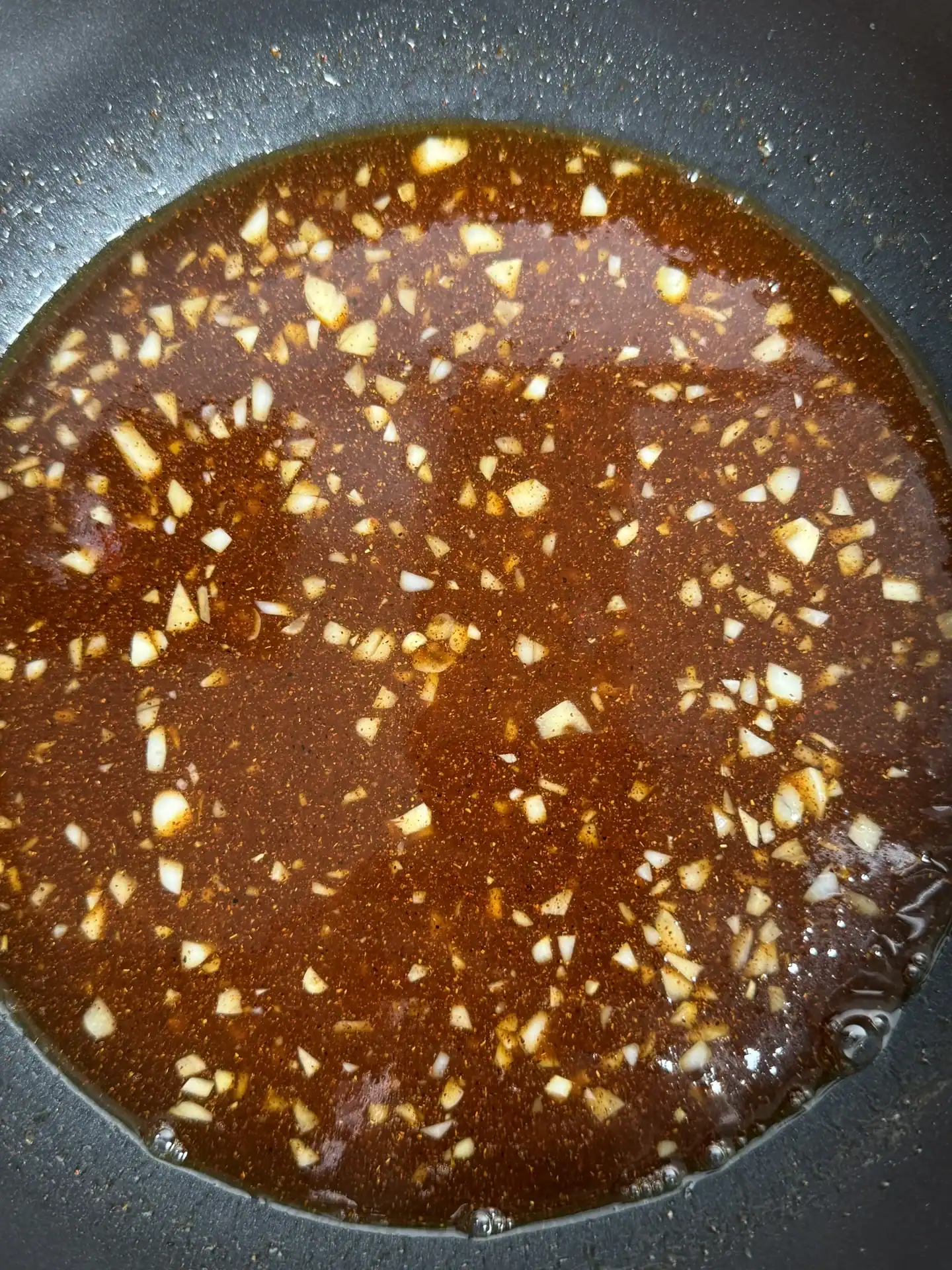 hot honey sauce with bits of minced garlic, cooking in a saucepan.