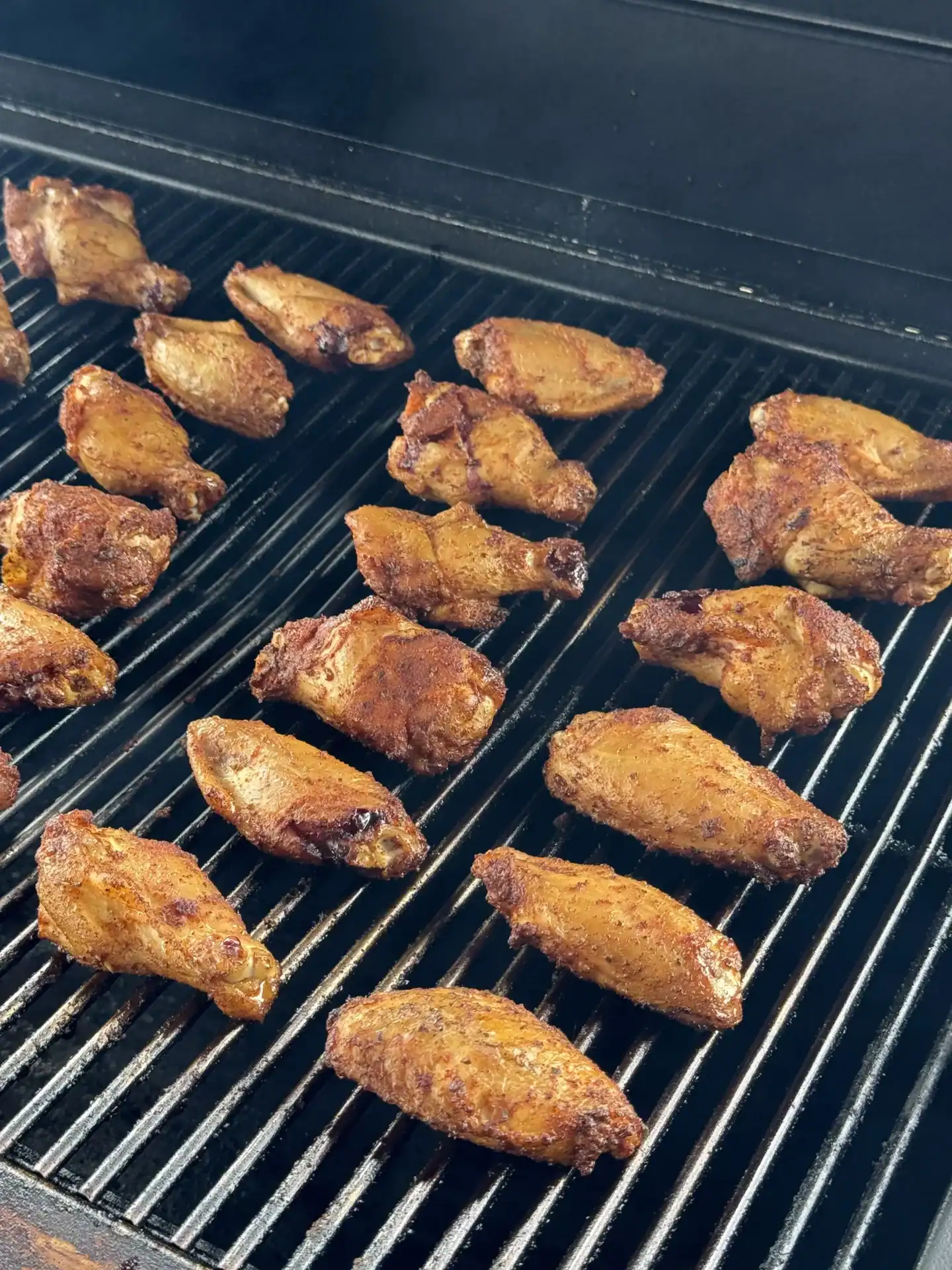 seasoned chicken wings arranged on a smoker.