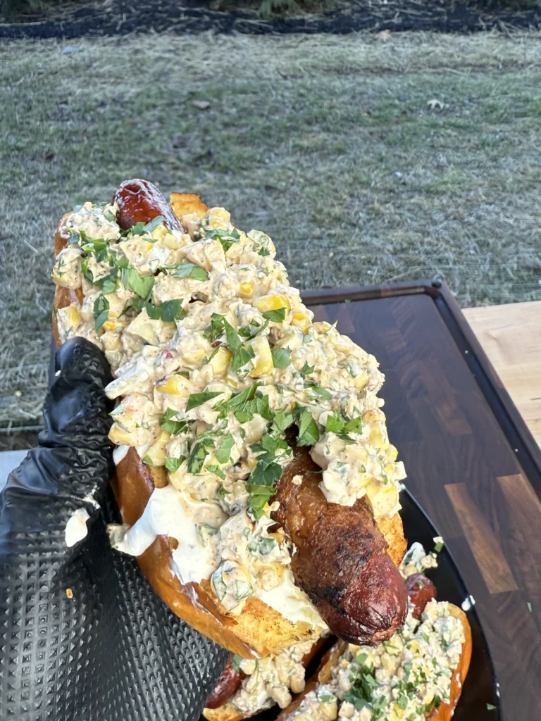 elote hot dog being held up with one hand