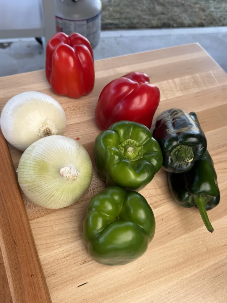 Red bell peppers, poblano peppers, and onions arranged neatly on a cutting board.