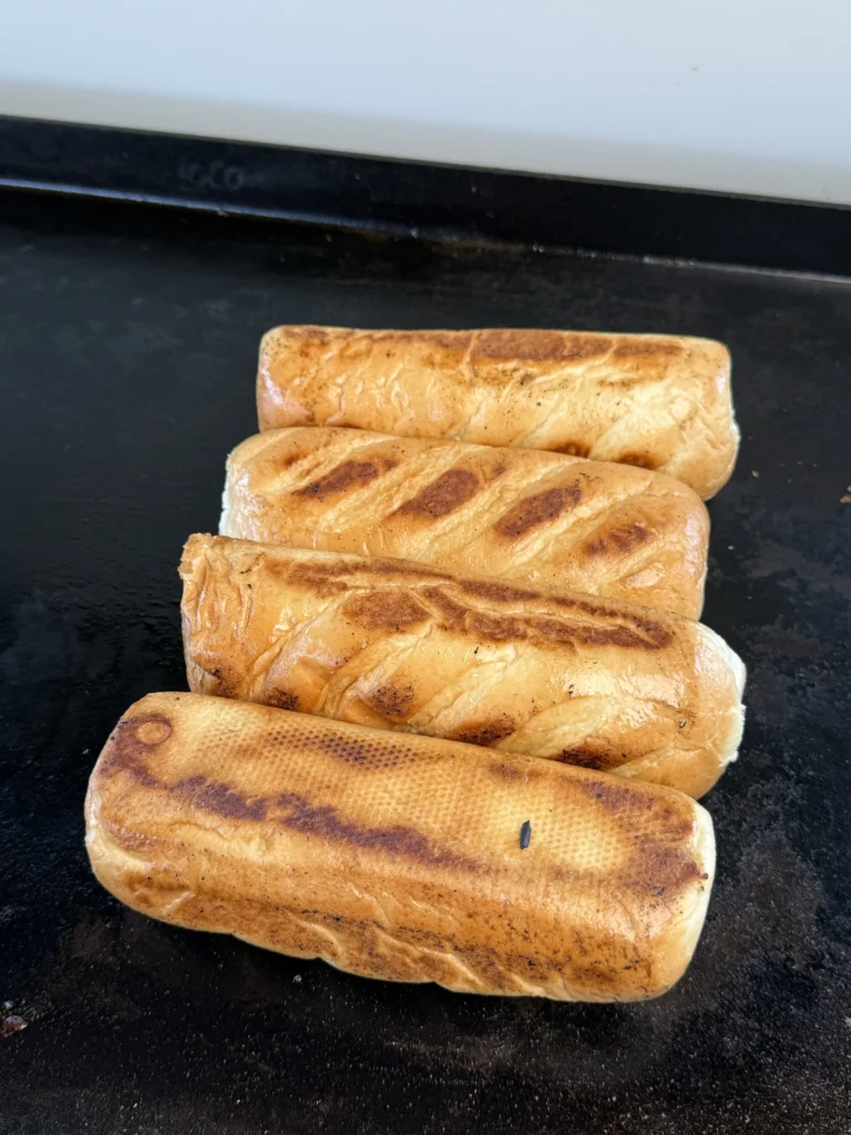 Buttered hoagie rolls being toasted to a golden brown on the griddle.