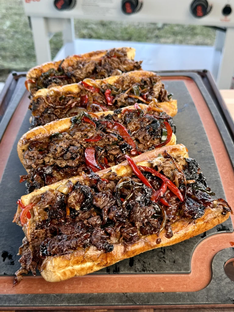 Three griddled cheesesteaks arranged on a cutting board, ready to be served.