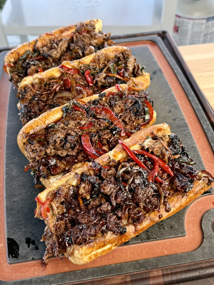 A plate with three griddled cheesesteaks on a cutting board