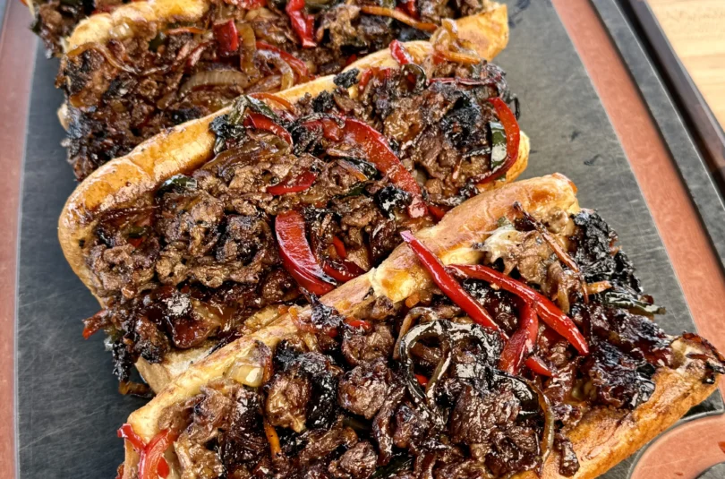 A plate with three griddled cheesesteaks on a cutting board