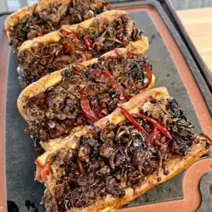 A plate with three griddled cheesesteaks on a cutting board