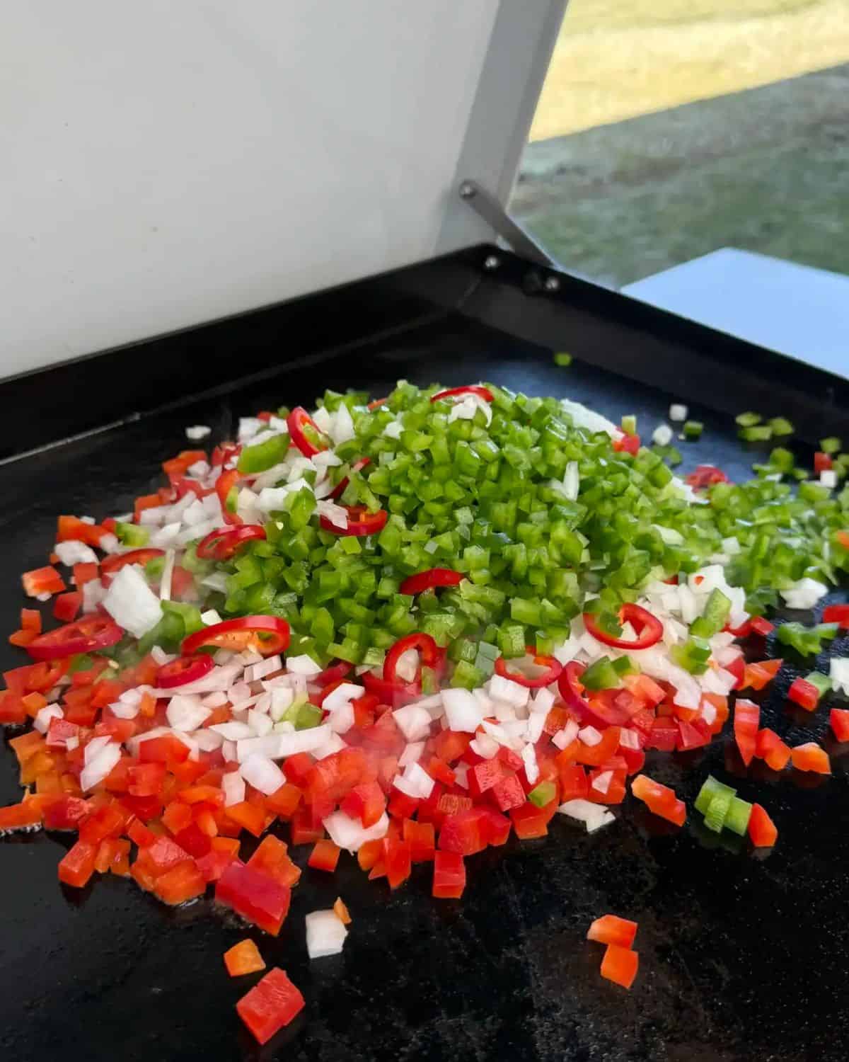 chopped bell peppers and onions being sauteed on a flat top griddle.