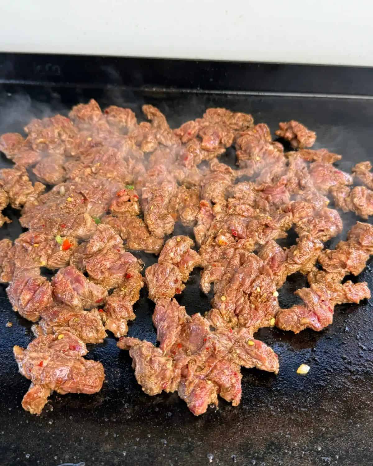 marinated steak being cooked on a flat top griddle.