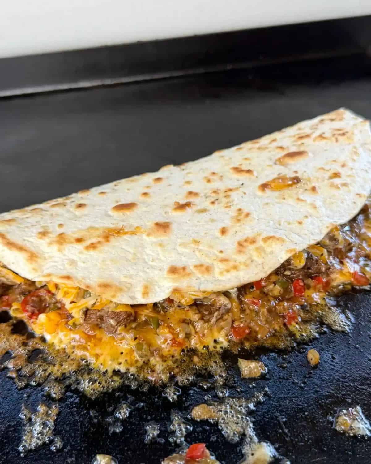 a flat top grill with a steak fajita quesadilla on it.