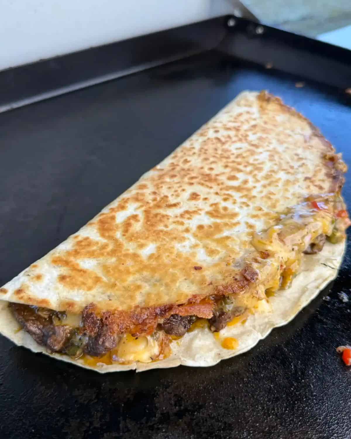 a golden brown steak quesadilla placed on a flat grill.
