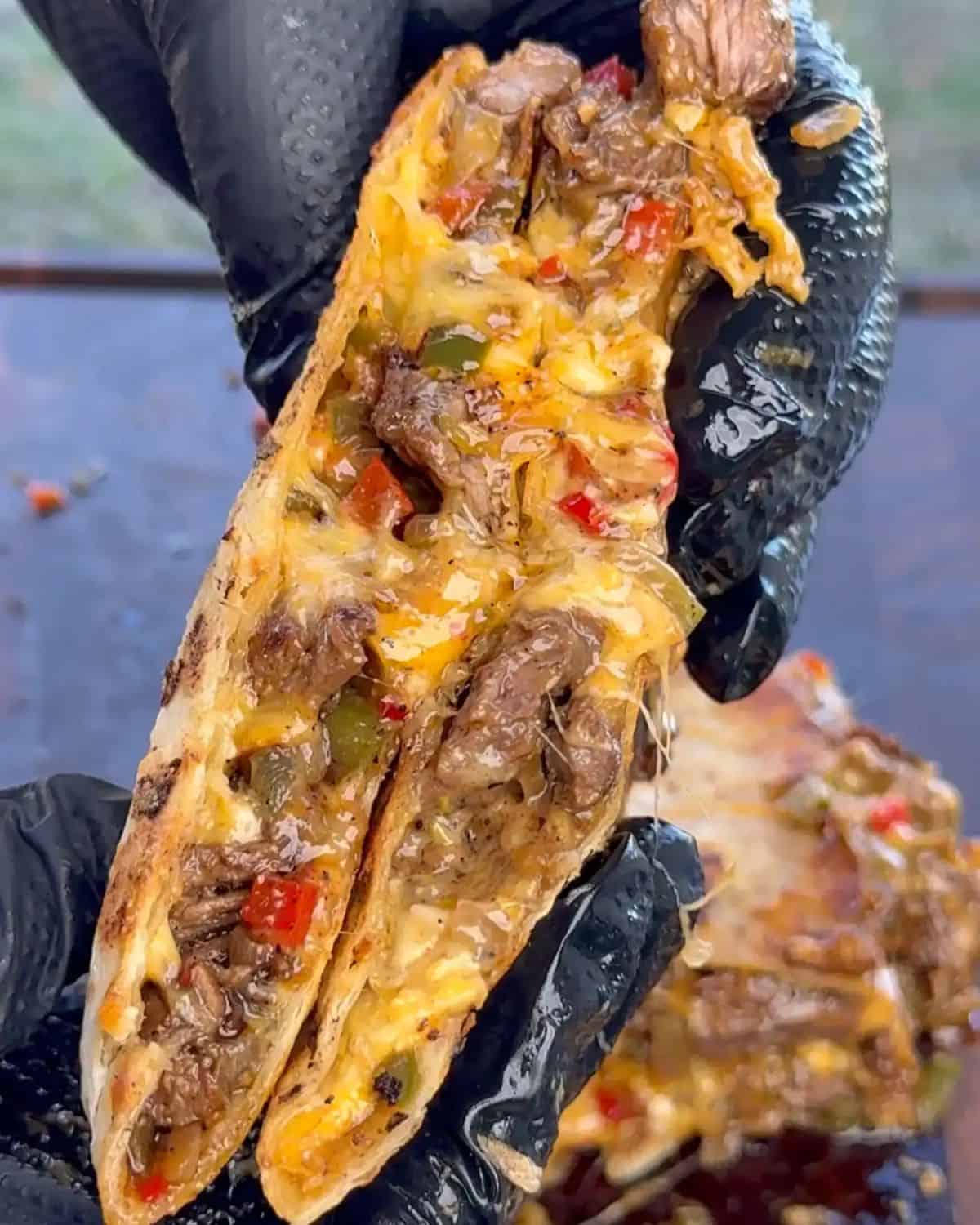 gloved hands holding a slice of chili lime steak fajita quesadilla with cheese oozing out. 