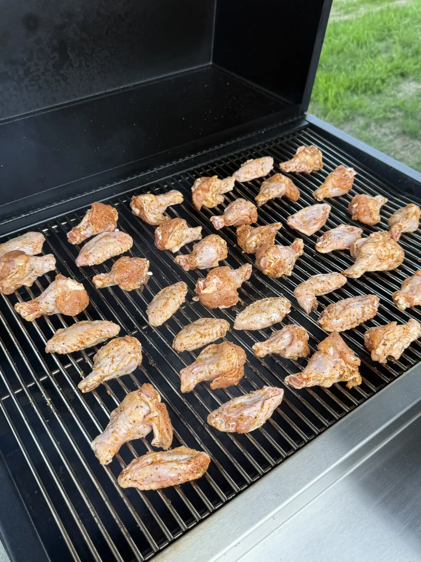 seasoned chicken wings placed on a smoker in an outdoor setting.