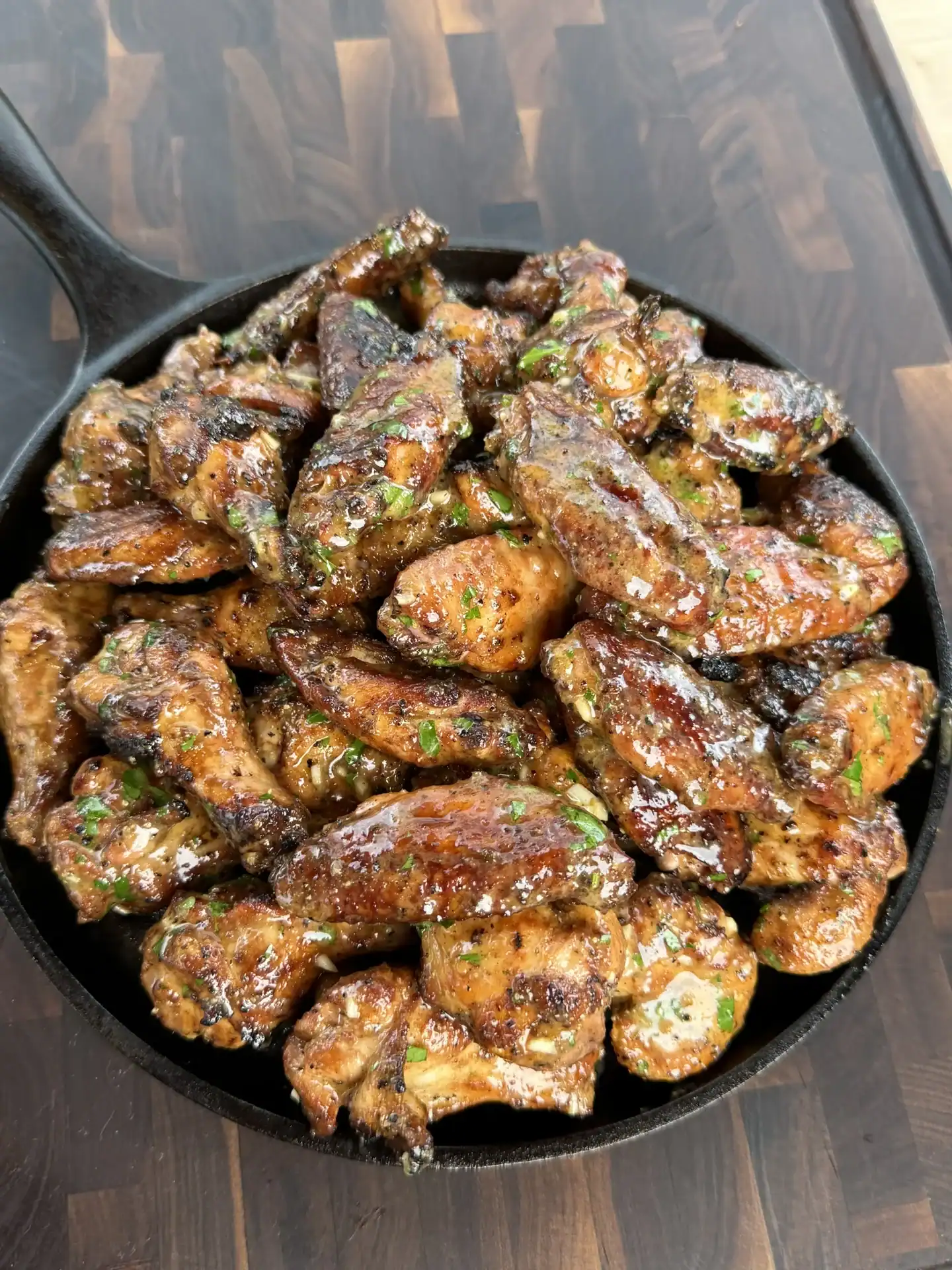 skillet stacked with smoked garlic lemon pepper chicken wings placed on a wooden table.