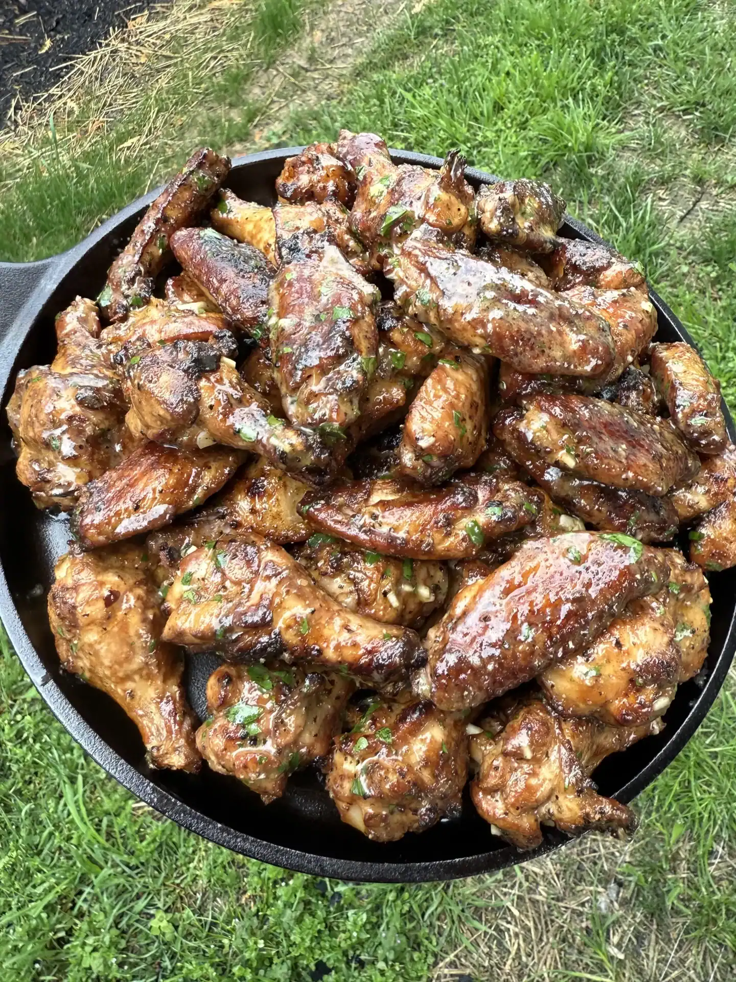 smoked chicken wings dressed in garlic lemon pepper butter in a skillet in an outdoor area.