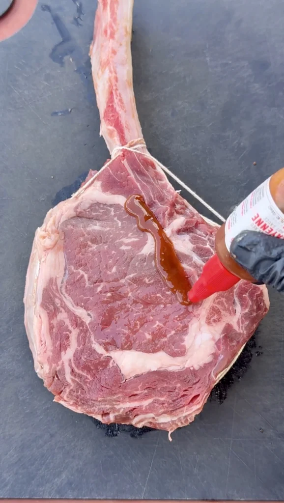 oil being drizzled over raw tomahawk steaks before seasoning