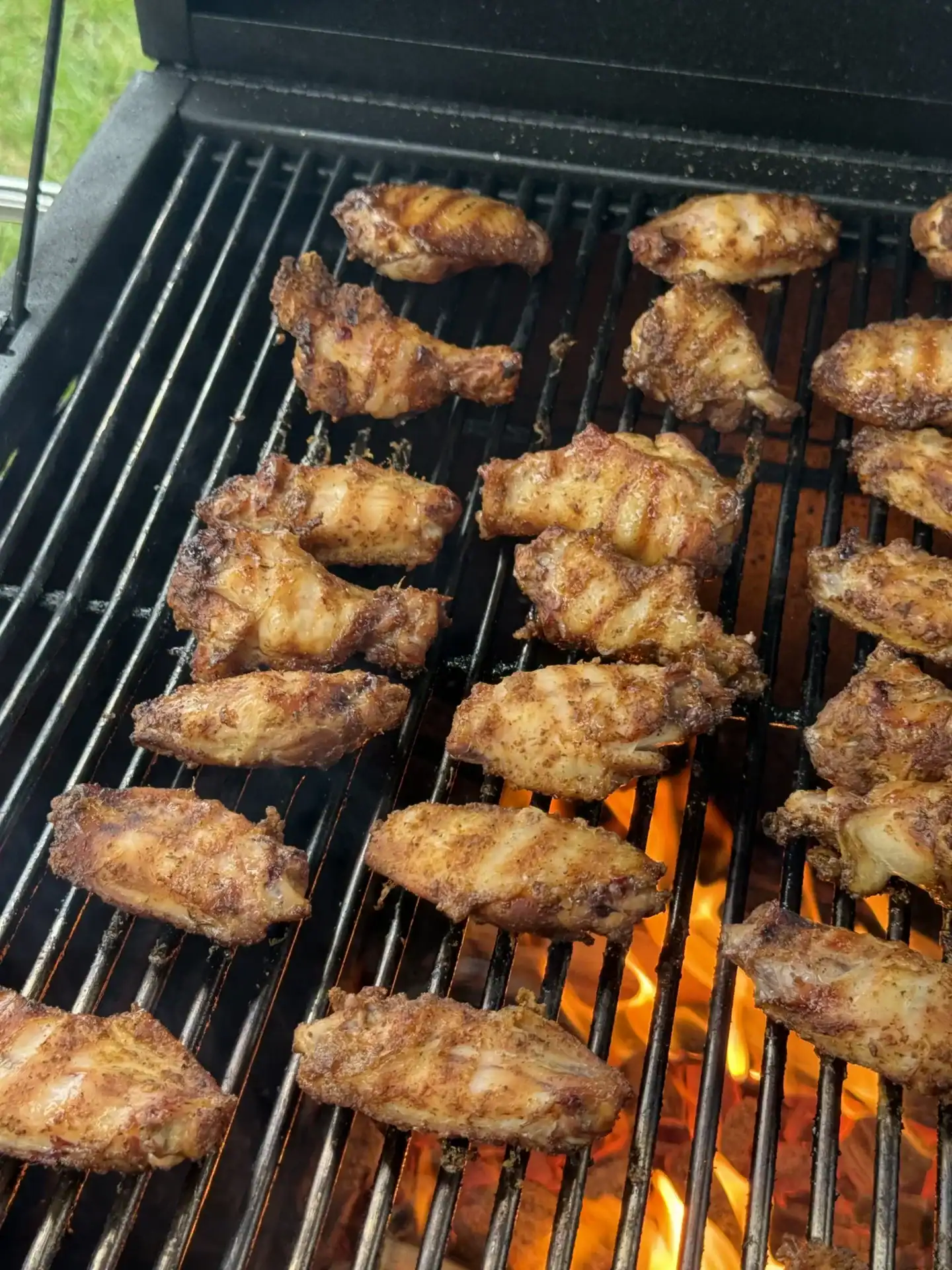 seasoned golden brown chicken wings being cooked on a grill.