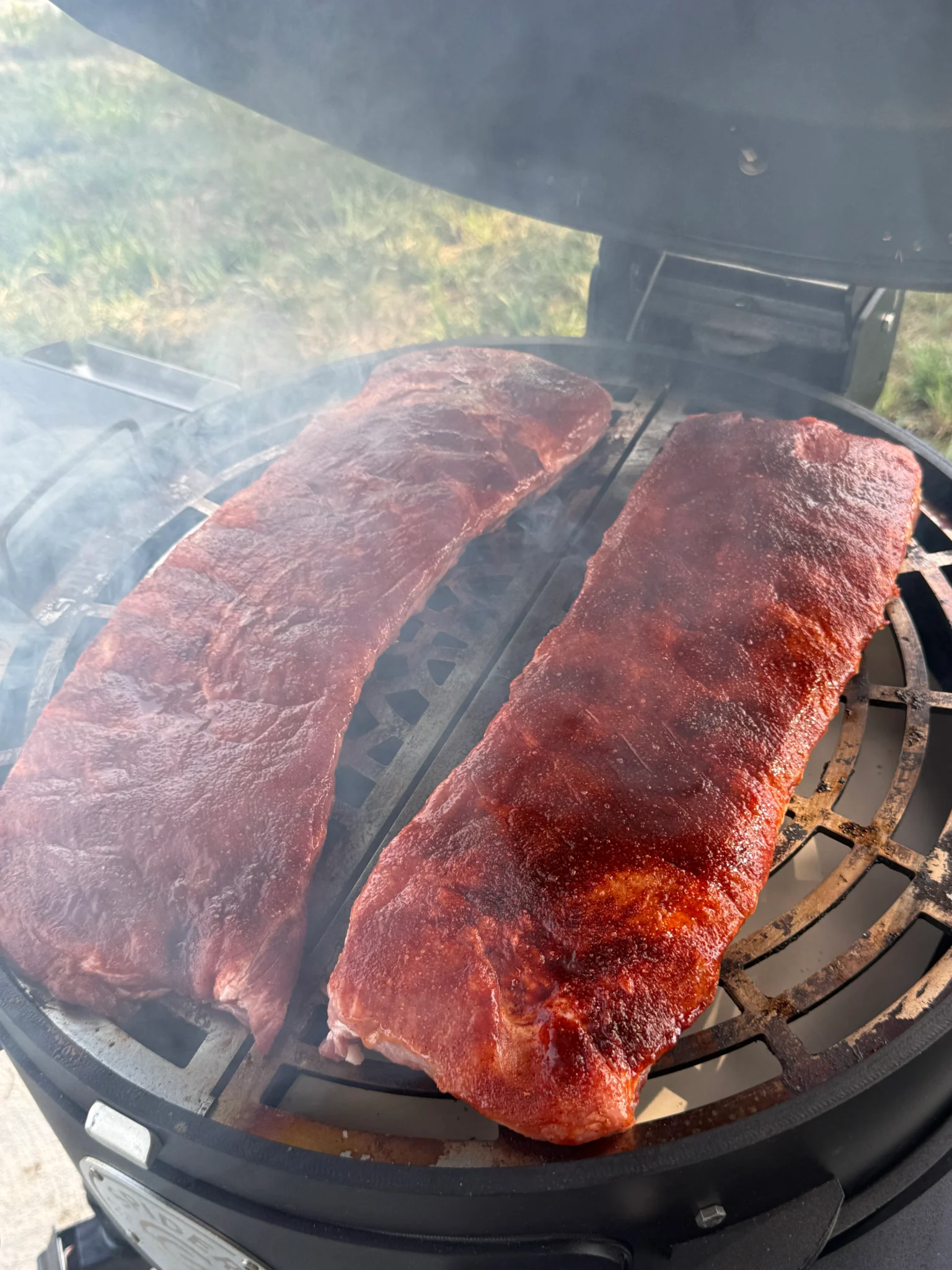 Baby back ribs smoking on a charcoal grill at 250 degrees with cherry wood chips for Cherry Dr Pepper glazed ribs