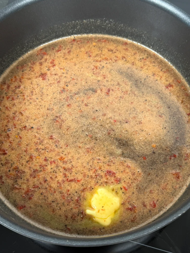 Finished Cherry Dr Pepper chipotle glaze in saucepan with butter being stirred in for final shine