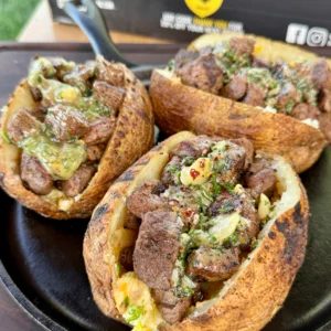 Completed grilled steak bite loaded baked potatoes garnished with fresh chives and drizzled with garlic herb butter on serving plates
