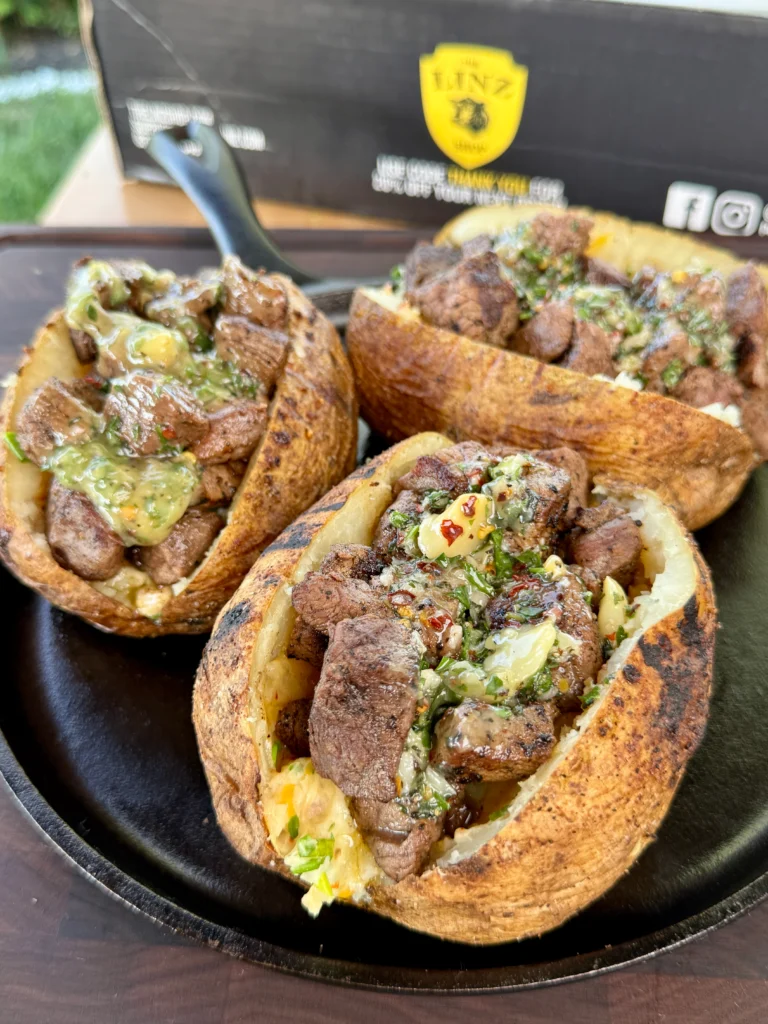 Completed grilled steak bite loaded baked potatoes garnished with fresh chives and drizzled with garlic herb butter on serving plates
