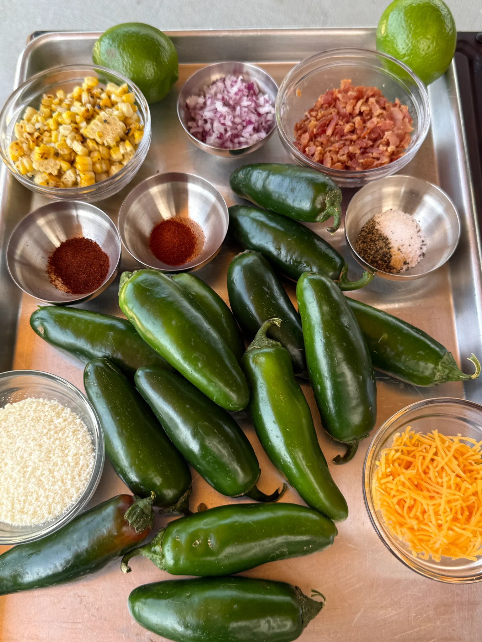 Raw ingredients for elote jalapeƱo poppers including fresh jalapeƱos, Cotija cheese, bacon, and corn