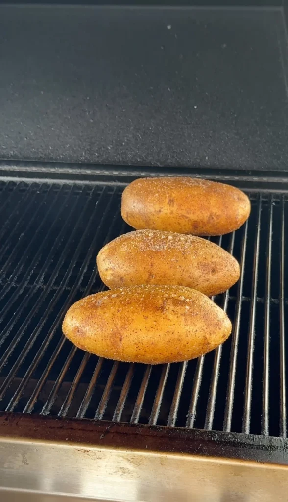 Russet potatoes wrapped in foil cooking on grill grates over indirect heat for perfect steakhouse-style baked potatoes