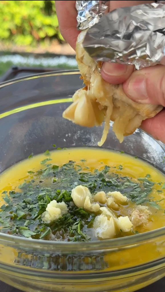 Garlic herb butter being prepared in small saucepan with melted butter, minced garlic, and fresh herbs like parsley and thyme