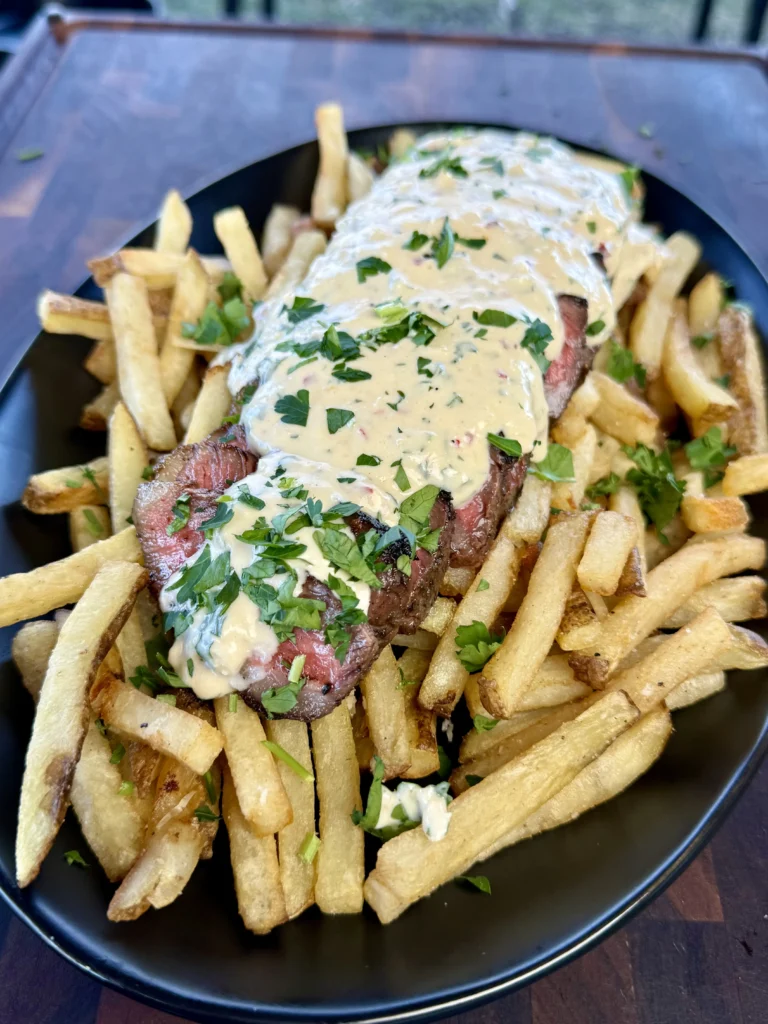 grilled steak on top of fries with garlic sauce