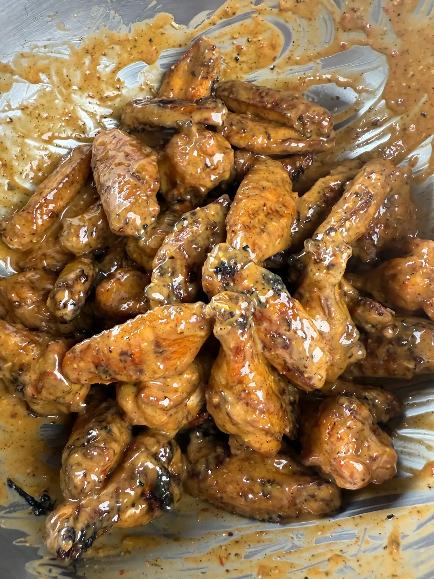 grilled chicken wings tossed in a spicy garlic Parmesan sauce in a stainless steel bowl.