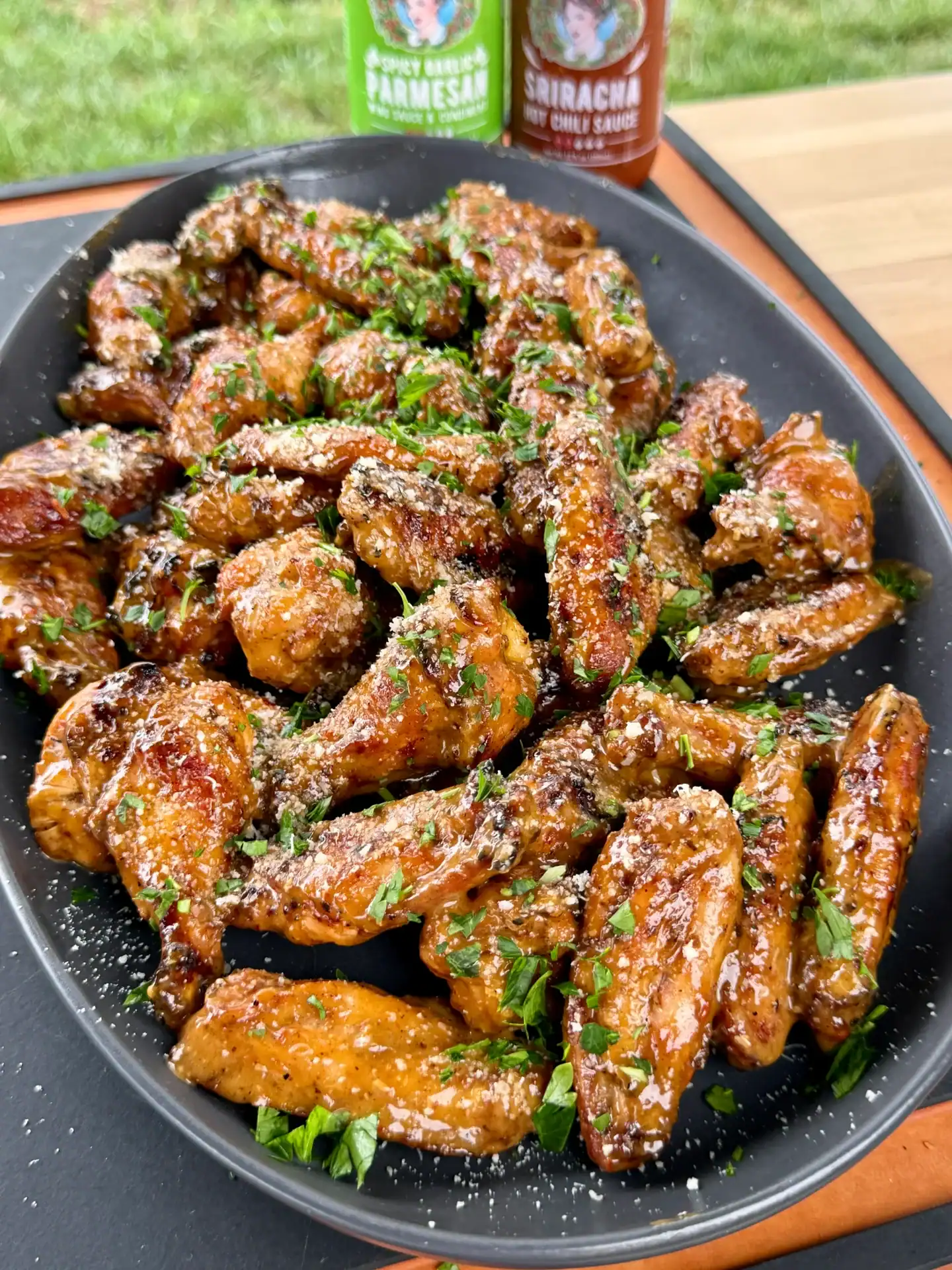 spicy garlic Parmesan chicken wings on a serving plate, topped with chopped parsley. 