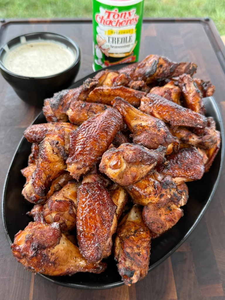 Smoked and grilled Creole chicken wings with Tony's ranch dip on a serving platter, showing crispy golden-brown skin and vibrant seasoning