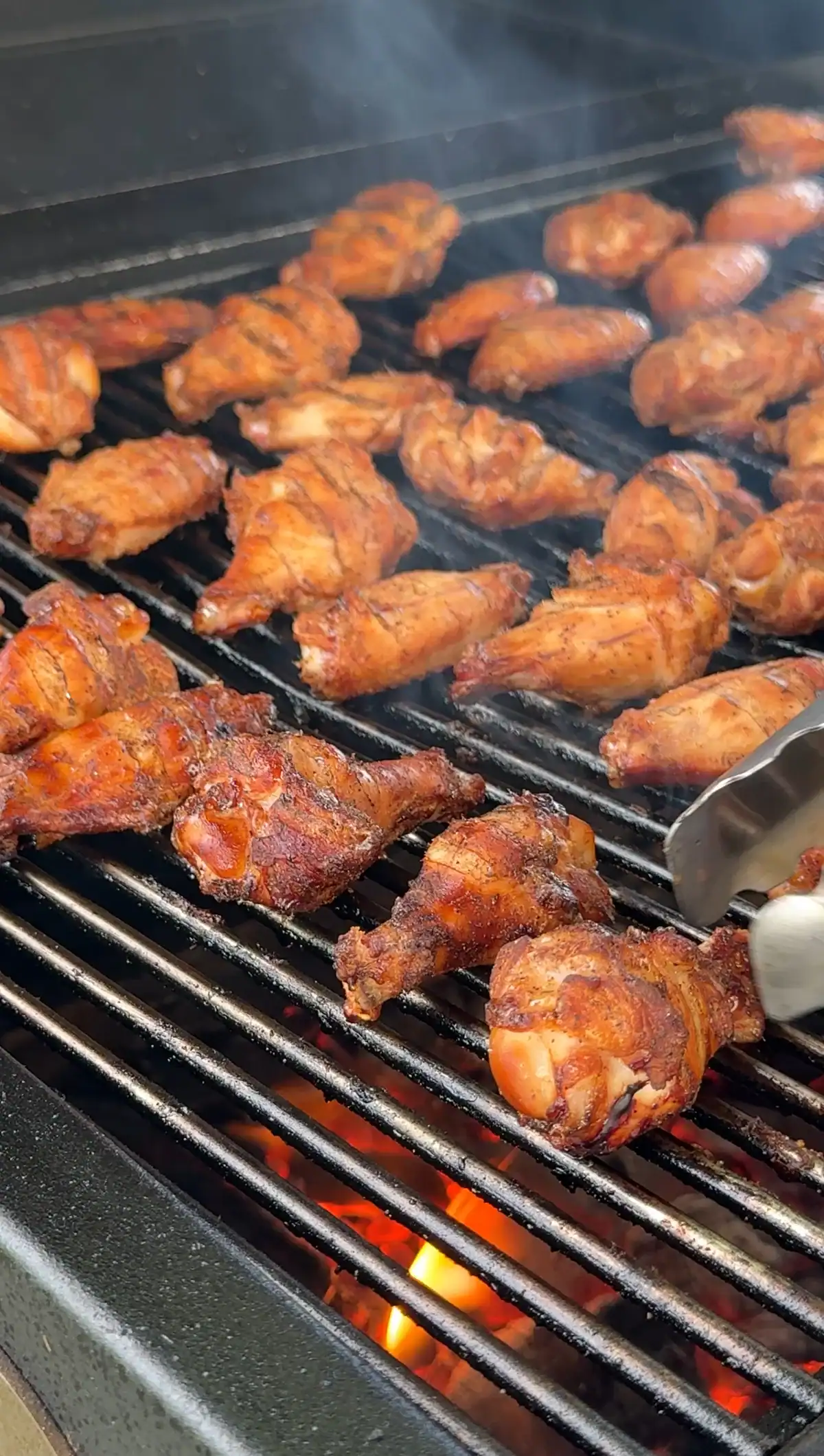 smoked Creole chicken wings being flipped over on a smoker.