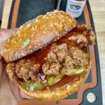 fried chicken sandwich being held over a cutting board