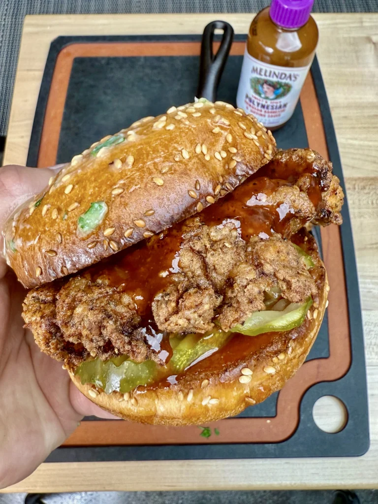 fried chicken sandwich being held over a cutting board