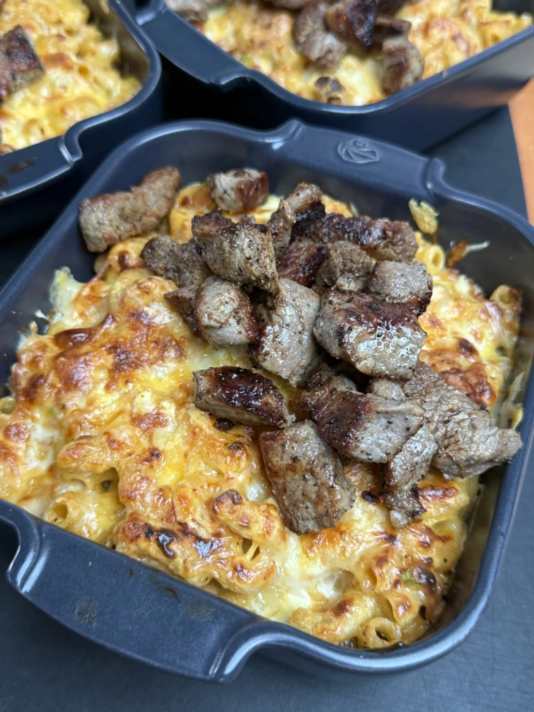 Completed steak bites loaded mac and cheese in serving dish topped with seared steak, crispy bacon