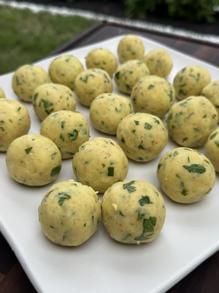  Uniformly shaped potato croquette balls with visible herbs arranged on white plate, demonstrating proper forming technique before breading