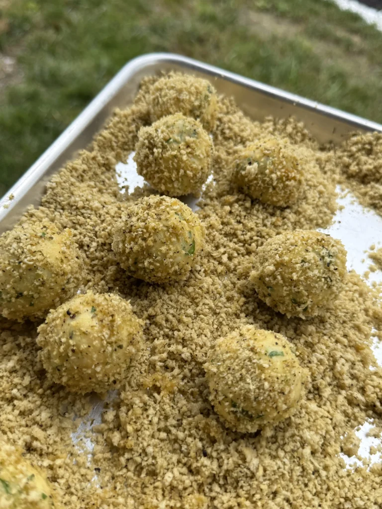Detailed view of breadcrumb-coated potato croquettes in tray showing even coating coverage and proper preparation for frying